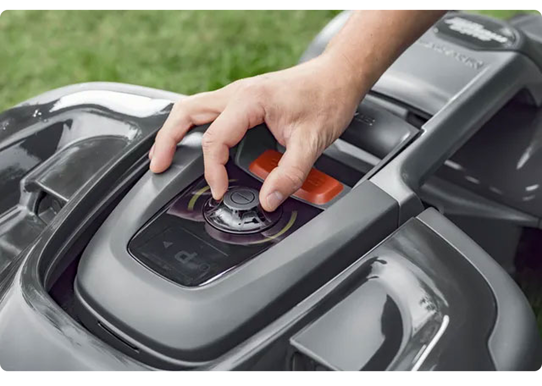 Close-up of a hand pressing the rotary control dial on a Husqvarna mower